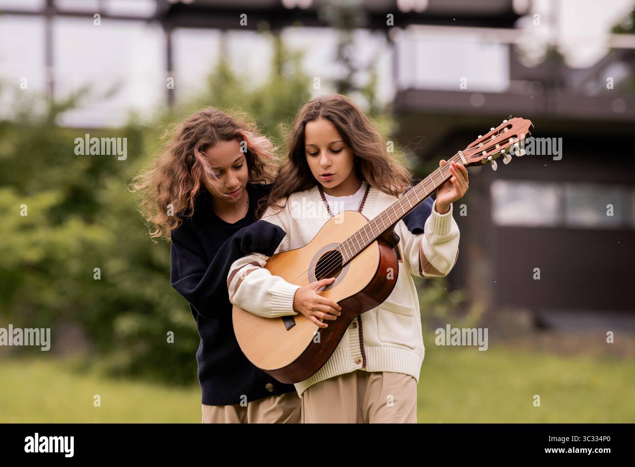 Zwei Zwillingsmädchen mit lockigem Haar spielen auf einer Gitarre und haben Spaß Stockfoto