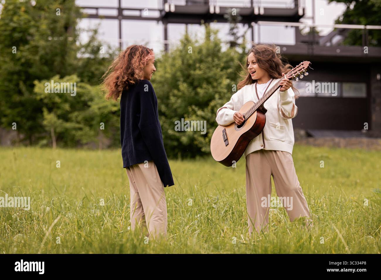 Zwei Zwillingsmädchen mit lockigem Haar spielen auf einer Gitarre und haben Spaß Stockfoto