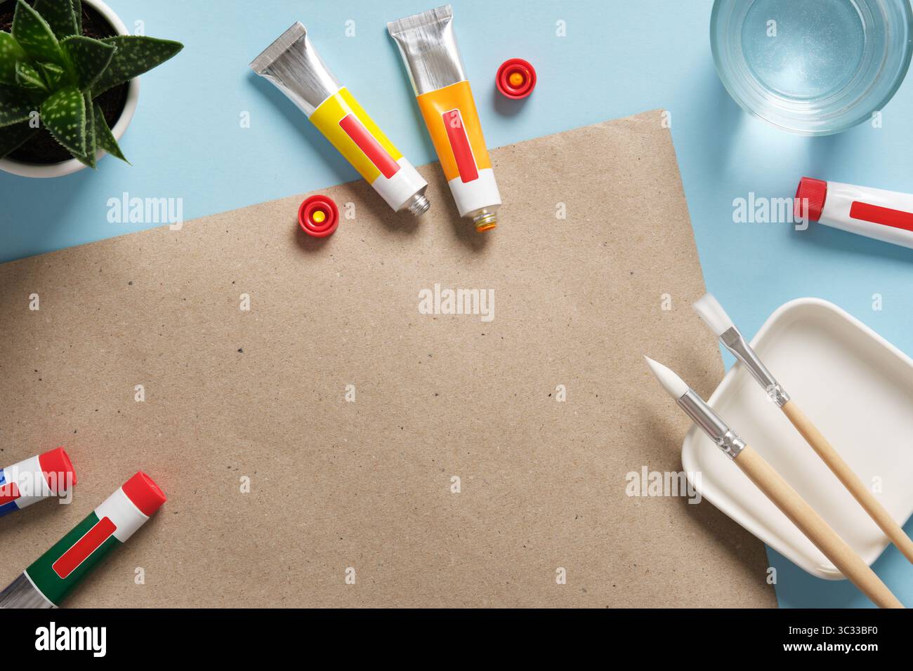 Vorbereitung auf das Zeichnen. Tuben aus Acrylfarbe, Pinsel, ein Glas Wasser auf blauem Hintergrund. Platzieren für Ihren Text. Stockfoto