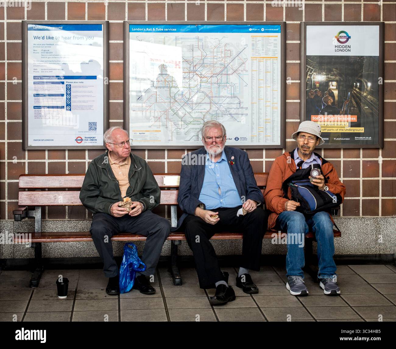 Drei Passagiere sitzen auf einer Bank in der Acton Town U-Bahn-Station, London, Großbritannien Stockfoto