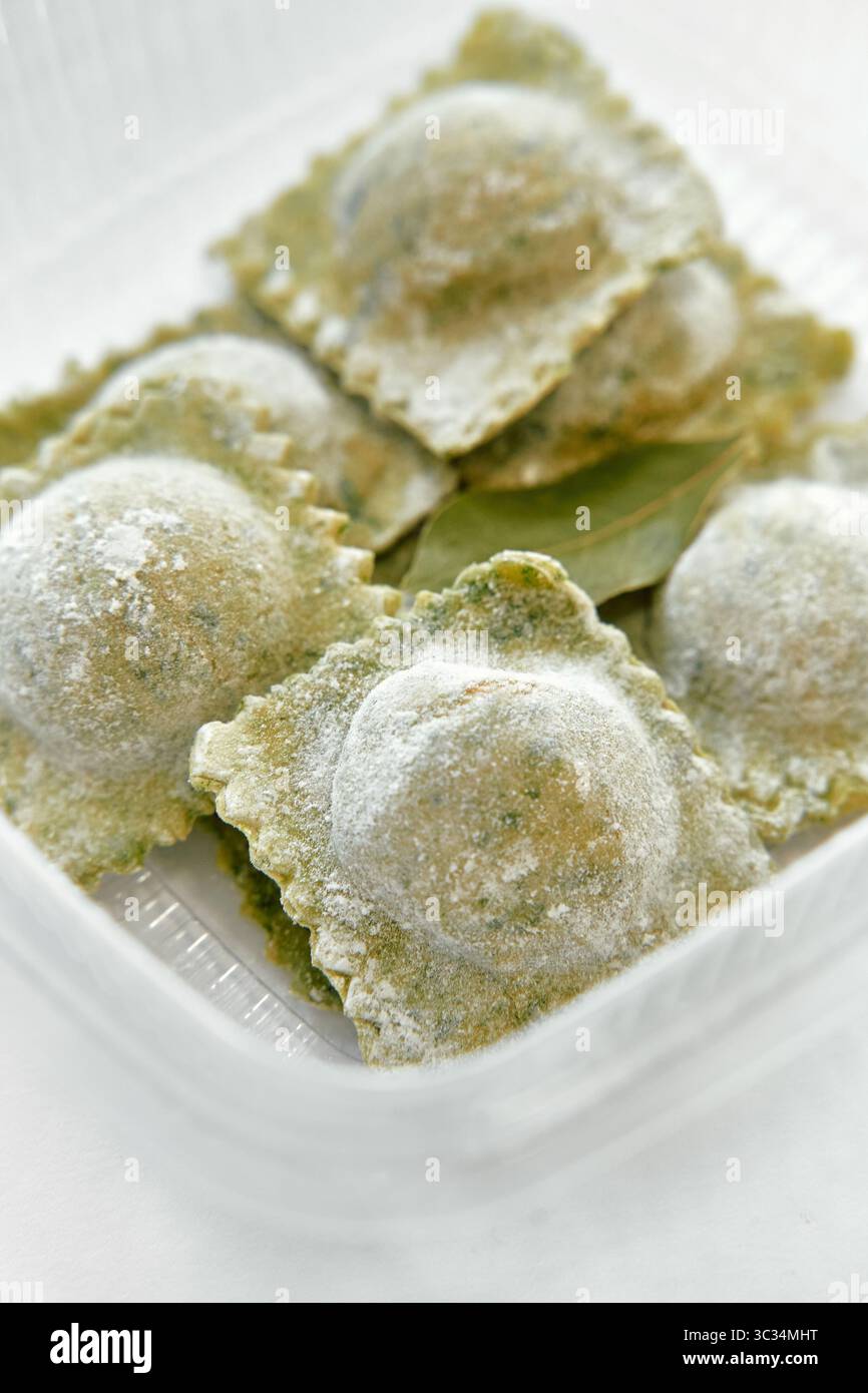 Eine Nahaufnahme des frisch zubereiteten grünen Ravioli in einem Behälter mit aromatischen Lorbeerblättern und einer leichten Staubfüllung von Mehl Stockfoto