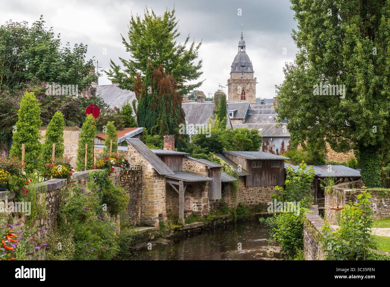 Die Waschhäuser der Kais von La Sienne und der Glockenturm der Kirche Notre-Dame unter stürmischem Himmel in Villedieu-les-Poêles in der Normandie, Frankreich Stockfoto