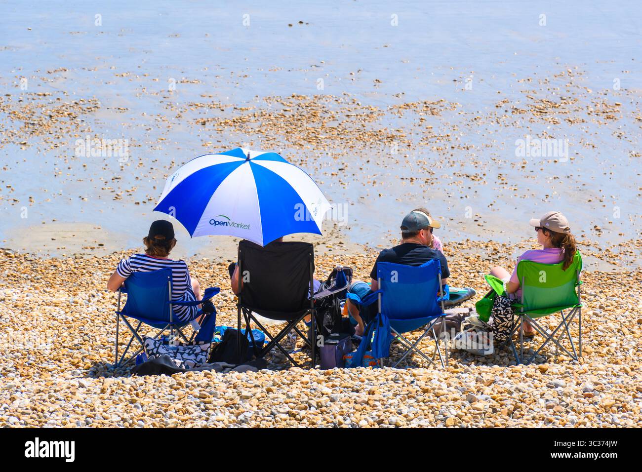 Lyme Regis, Dorset, Großbritannien. Juli 2025. Wetter in Großbritannien: Eine Familie genießt die heiße Sonne unter einem Sonnenschirm am Strand im Badeort Lyme Regis zu Beginn der Schulferien. Quelle: Celia McMahon/Alamy Live News Stockfoto