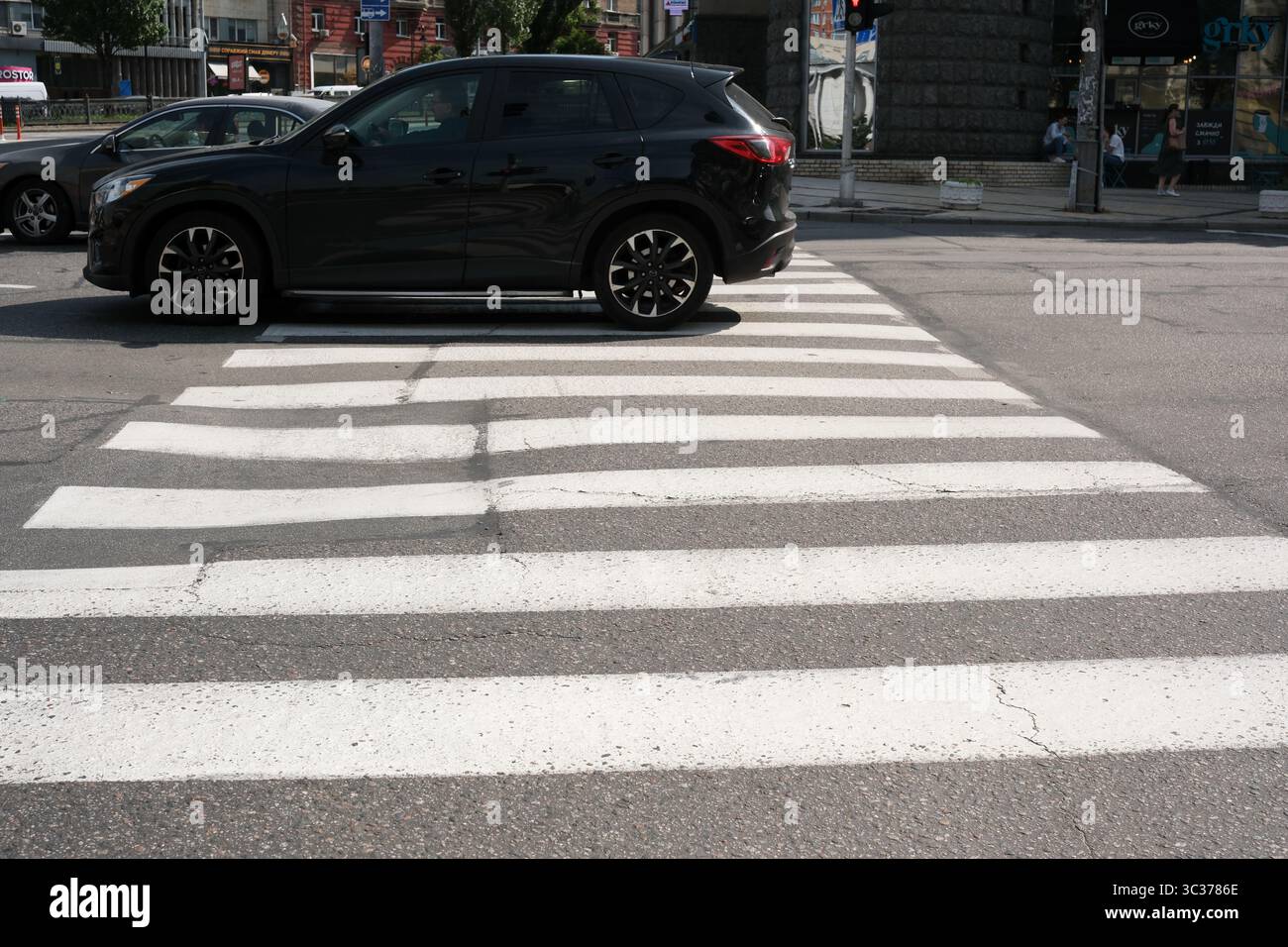 Ein elegantes schwarzes Auto fährt bei Tageslicht über Zebrastreifen in den belebten Straßen Kiews. Stockfoto