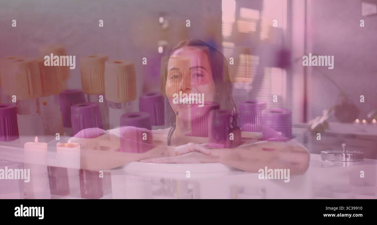 Eine Frau, die Badeanzug in der Badewanne im Spa-Raum trägt, mit Kerzen, Handtüchern, Fenster, Pflanze Stockfoto