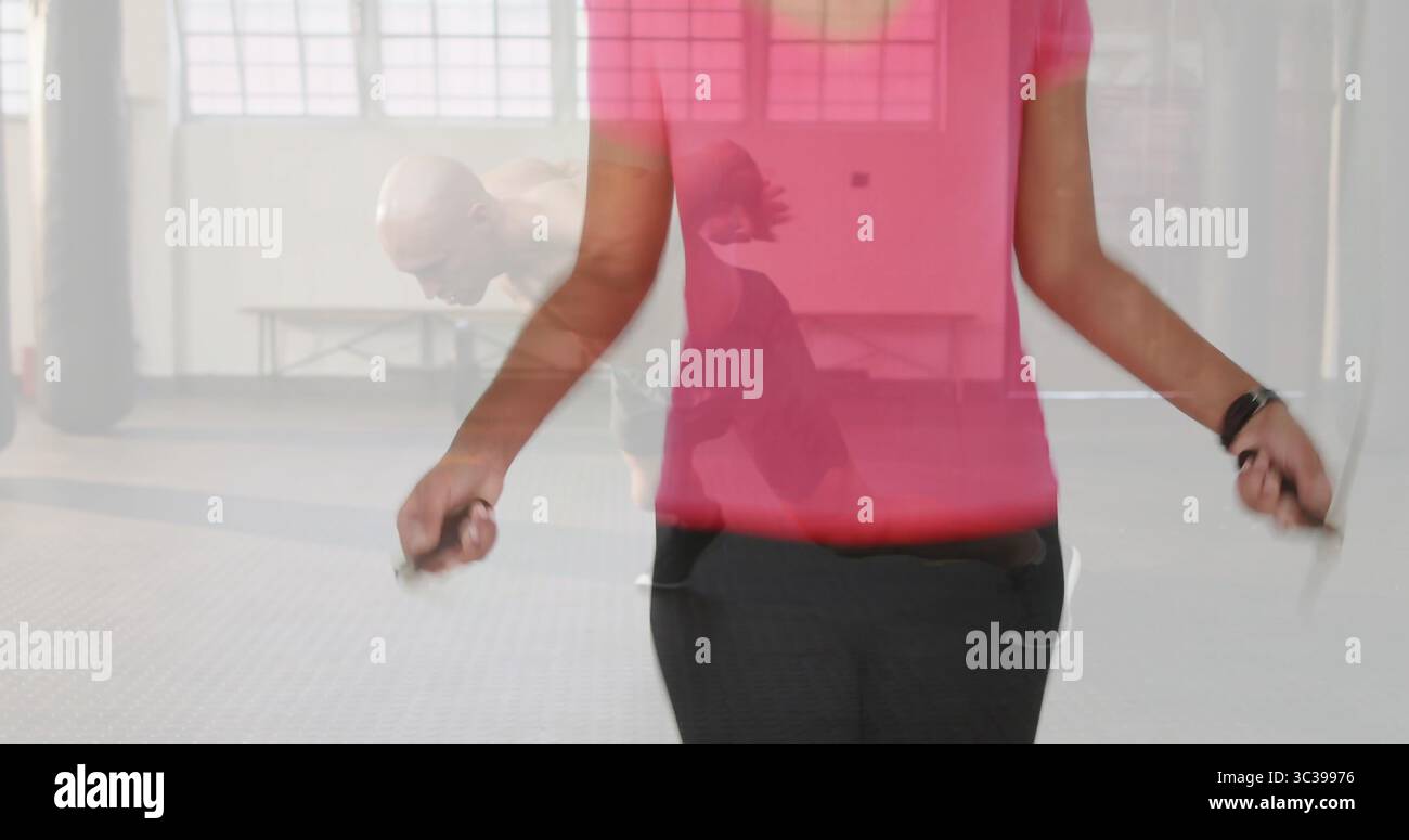 Afroamerikanerin mit rosafarbenem Oberteil mit Sprungseil im Fitnessstudio, mit Boxsäcken Stockfoto