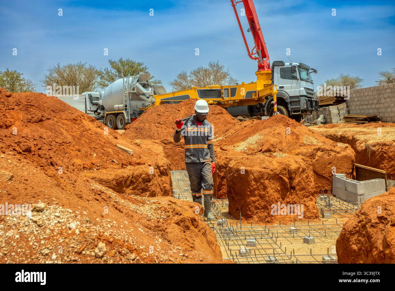 Afrikanischer Arbeiter, der auf einem Stahlstahlstahlstahlstahlstahl läuft, Graben für ein Haus auf der Baustelle, Betonmischwagen und ein Betonpumpenkran alles schwer Stockfoto