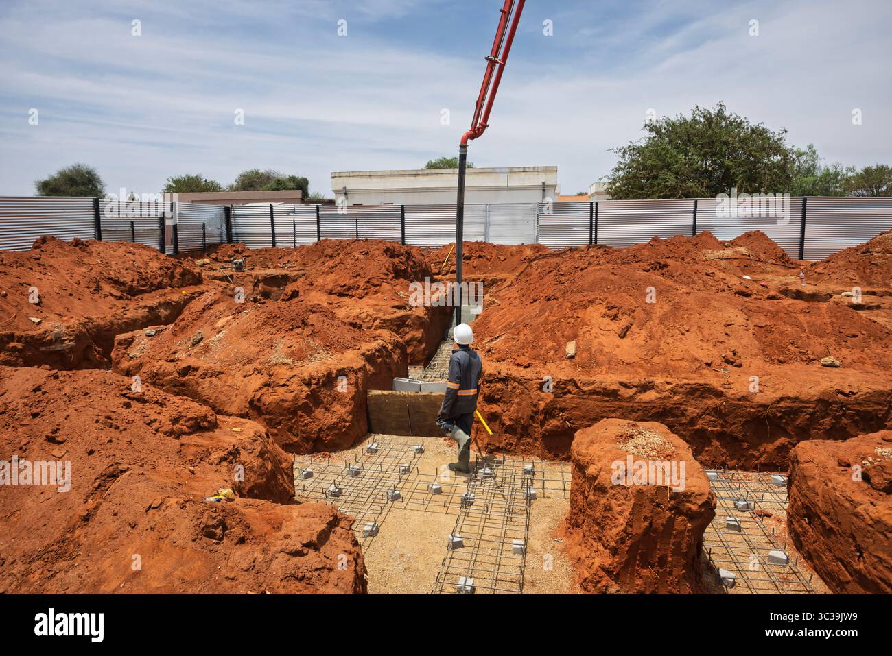 Afrikanischer Arbeiter, der auf einem Stahlstahlstahlstahl läuft, Graben für ein Haus auf der Baustelle, ein Betonpumpenkran, schwere Baumaschinen, Profi Stockfoto