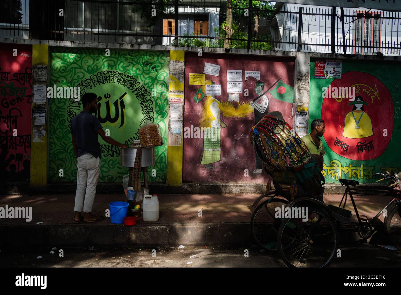 In Dhaka, Bangladesch, operiert ein einsamer Street Food-Händler in der Nähe eines lebendig bemalten Grafitti des Islam und der Jubelabscheu. Stockfoto