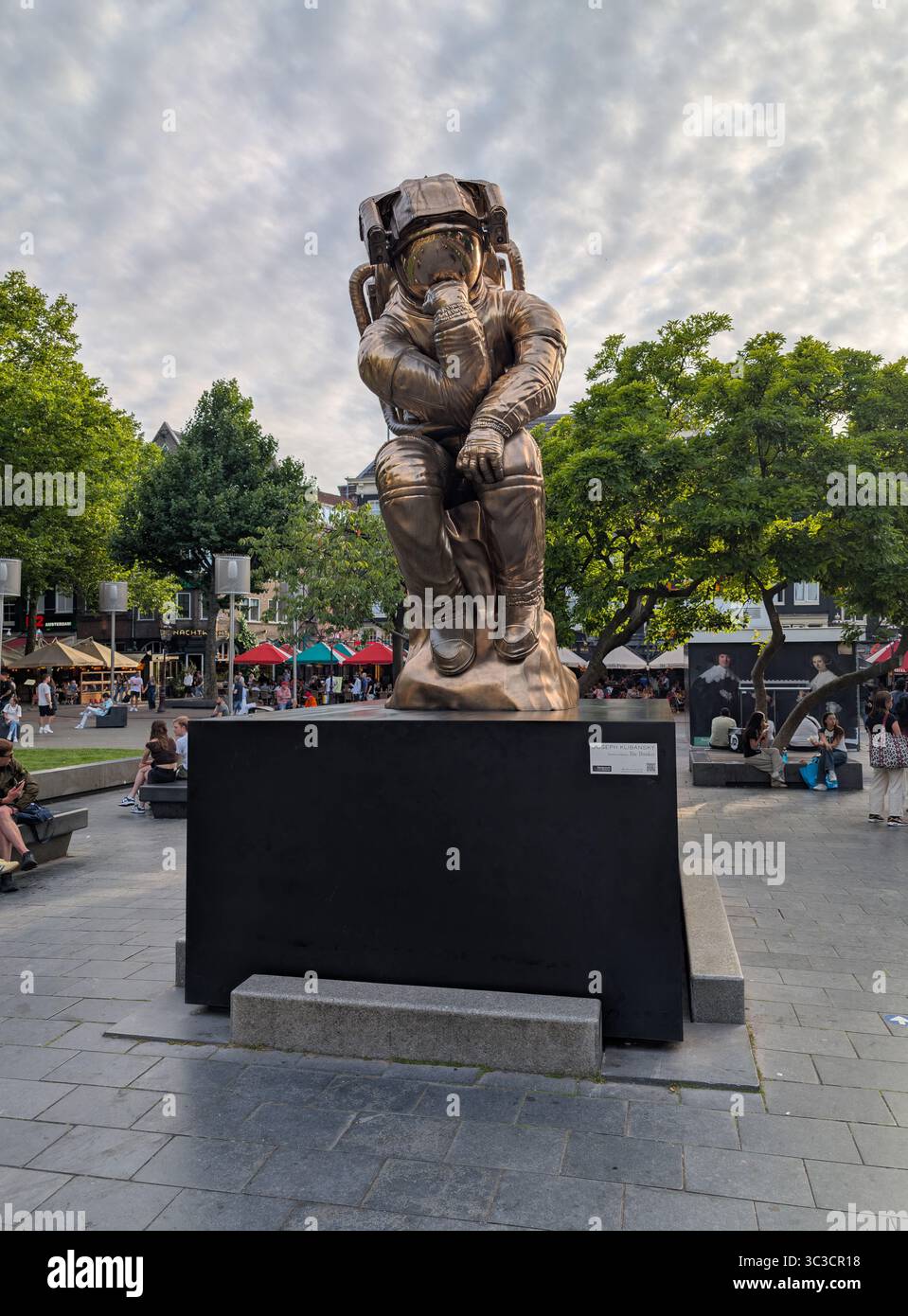 Das Kunstwerk von Joseph Klibansky zeigt einen Astronauten, der auf einem Sockel sitzt, der wie ein Stein aussieht. Sie befindet sich gegenüber einer Rembrandtstatue. Stockfoto
