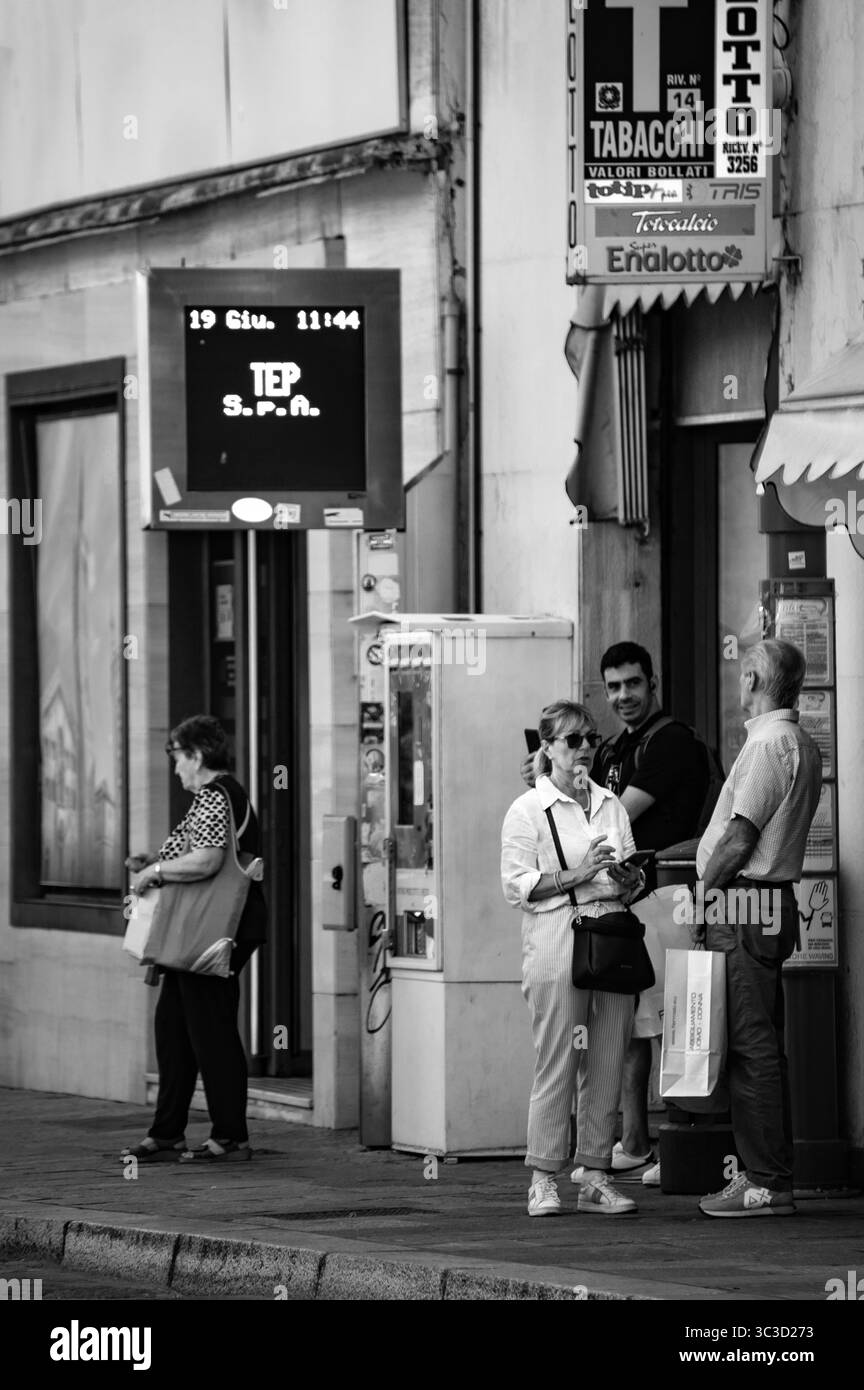 Stadtfotografie, die Pendler an einer Bushaltestelle mit Zeitanzeige und kommerziellen Schildern festhalten. Stockfoto