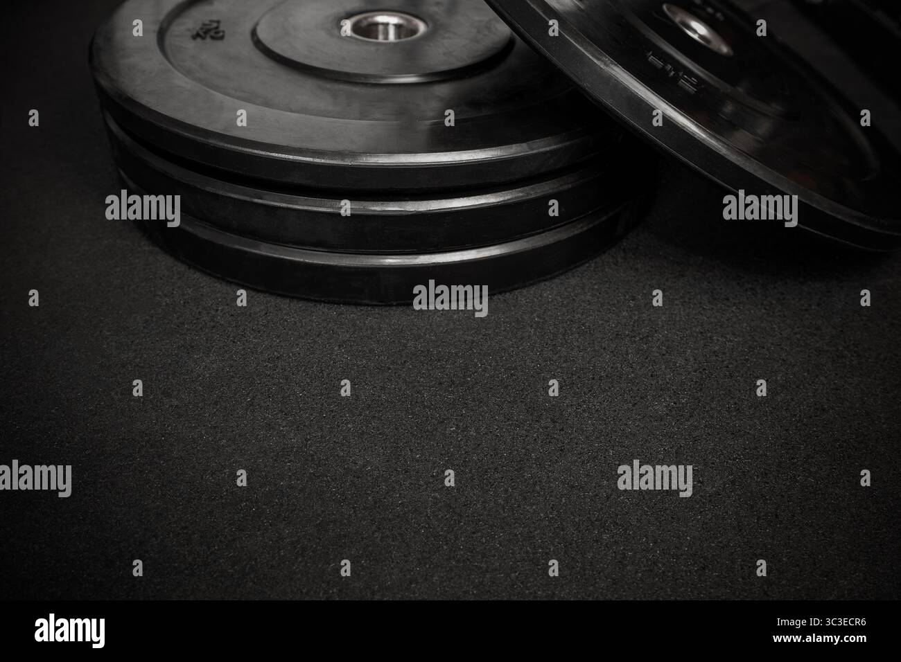 Hantelplatten auf einem schwarzen Fitnessboden vermitteln ein kraftvolles Bild von Krafttraining und Fitnessvorbereitung Stockfoto