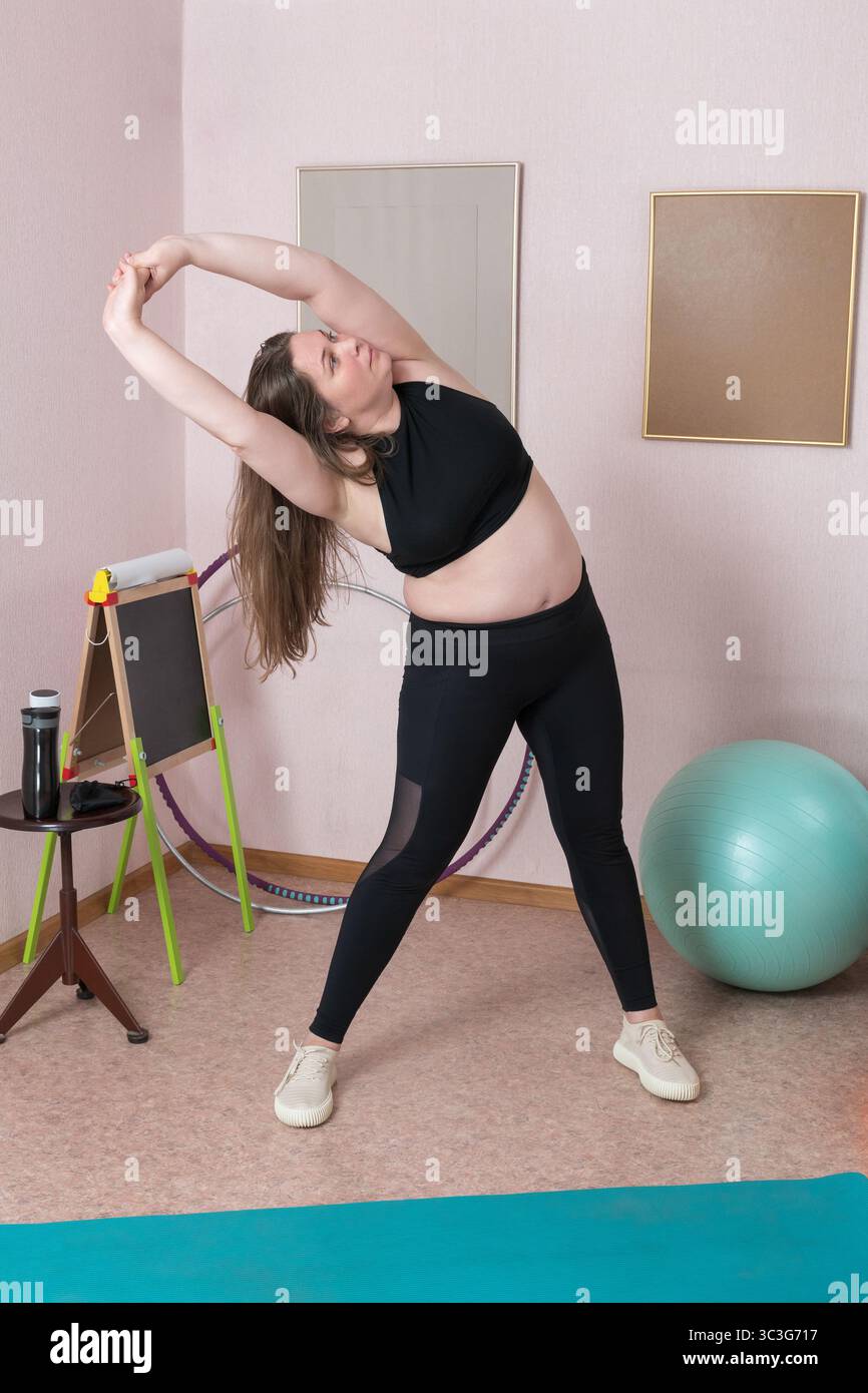 Gesamtlänge einer erwachsenen Frau, die eine dynamische laterale Beugung durchführt, mit erhobenen Armen in perfekter Haltung, Segment der häuslichen Pilatesroutine. Aa Stockfoto