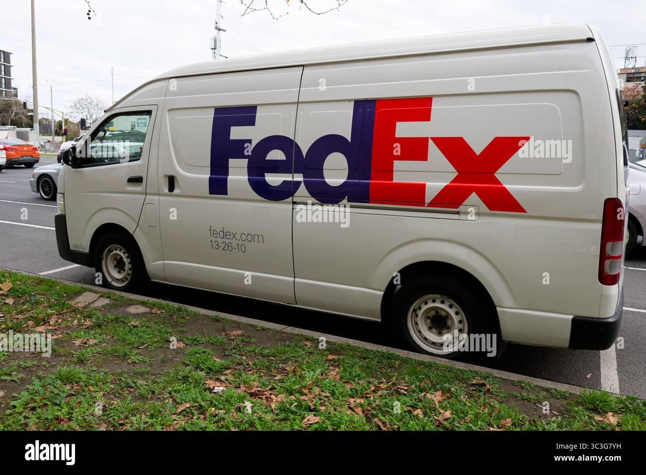 Seitenansicht eines weißen FedEx Lieferwagens, der an einem bewölkten Tag neben einer befahrenen Straße parkt Stockfoto
