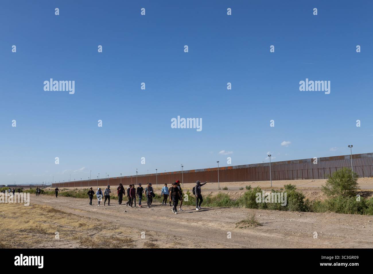 Migranten gehen am hoch aufragenden Zaun in Ciudad Juarez vorbei und symbolisieren die enormen Migrationsherausforderungen. Stockfoto