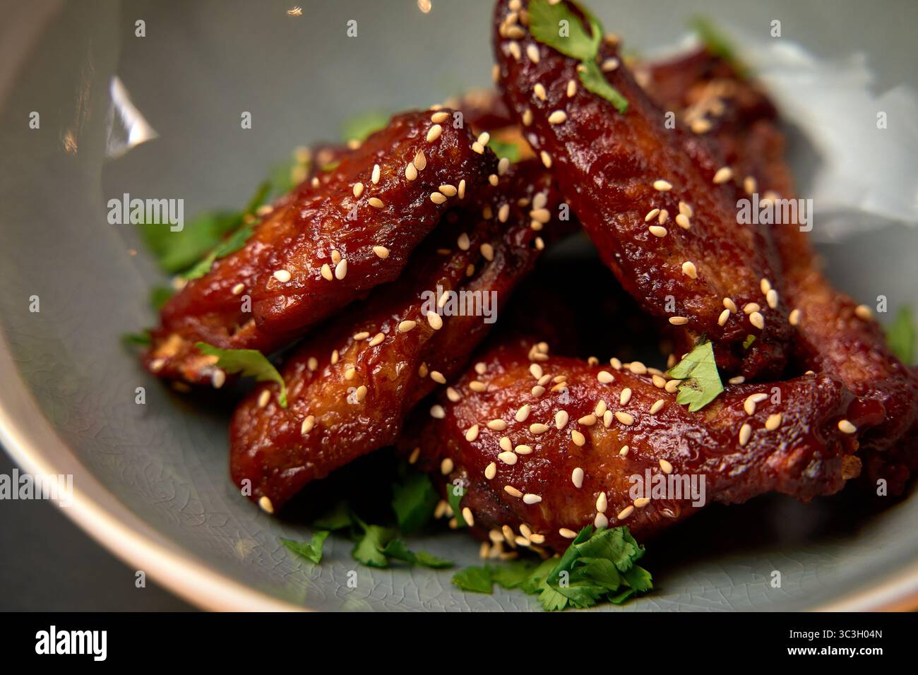 Saftige glasierte Chicken Wings mit Sesamsamen und frischem Koriander auf einer dekorativen Platte, perfekt für Partys oder Familientreffen Stockfoto