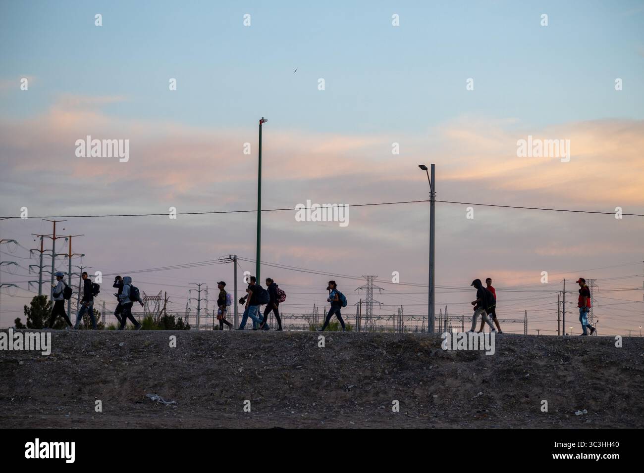 Menschen laufen in der Abenddämmerung in der Nähe von Stromleitungen an der Grenze zu Ciudad Juarez, was die Migrationsherausforderungen widerspiegelt. Stockfoto