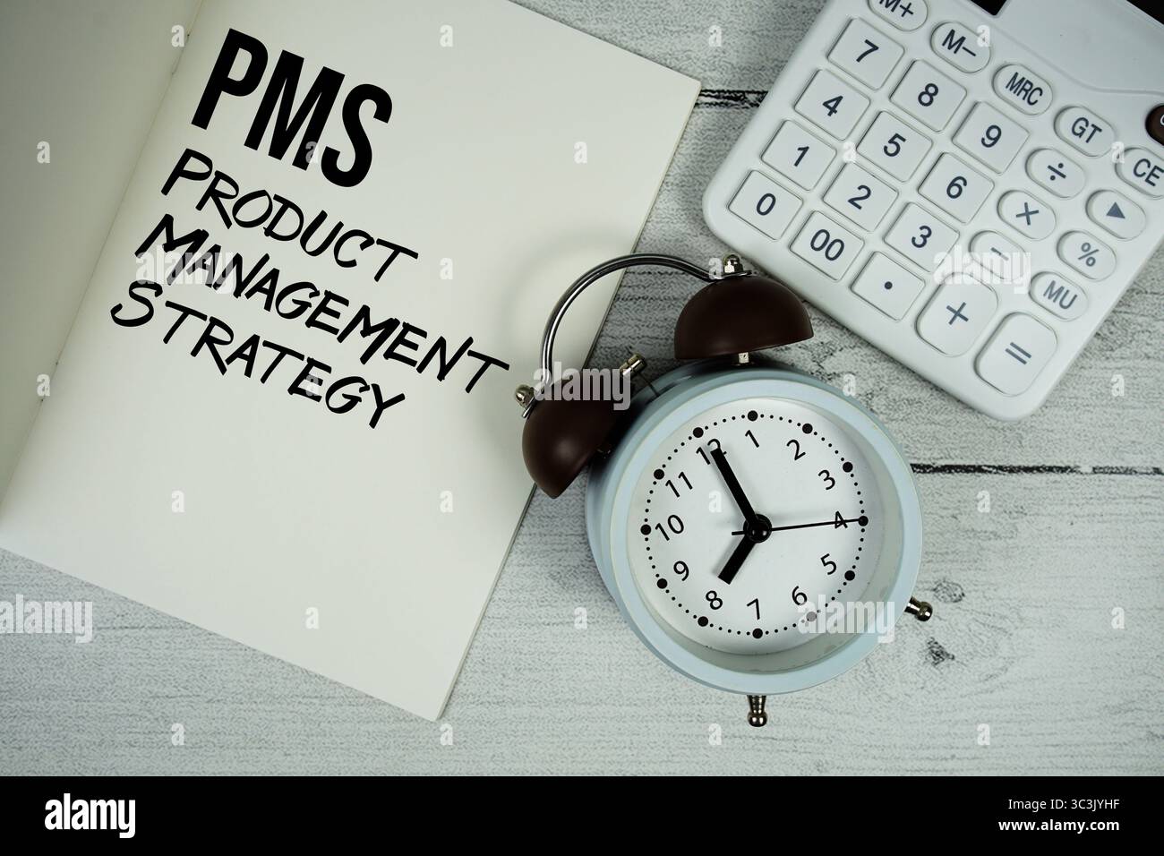 PMS-Produktmanagement-Strategietext auf Notizbuchseite auf Papier mit Wecker und Taschenrechner auf hölzernem Hintergrund Stockfoto