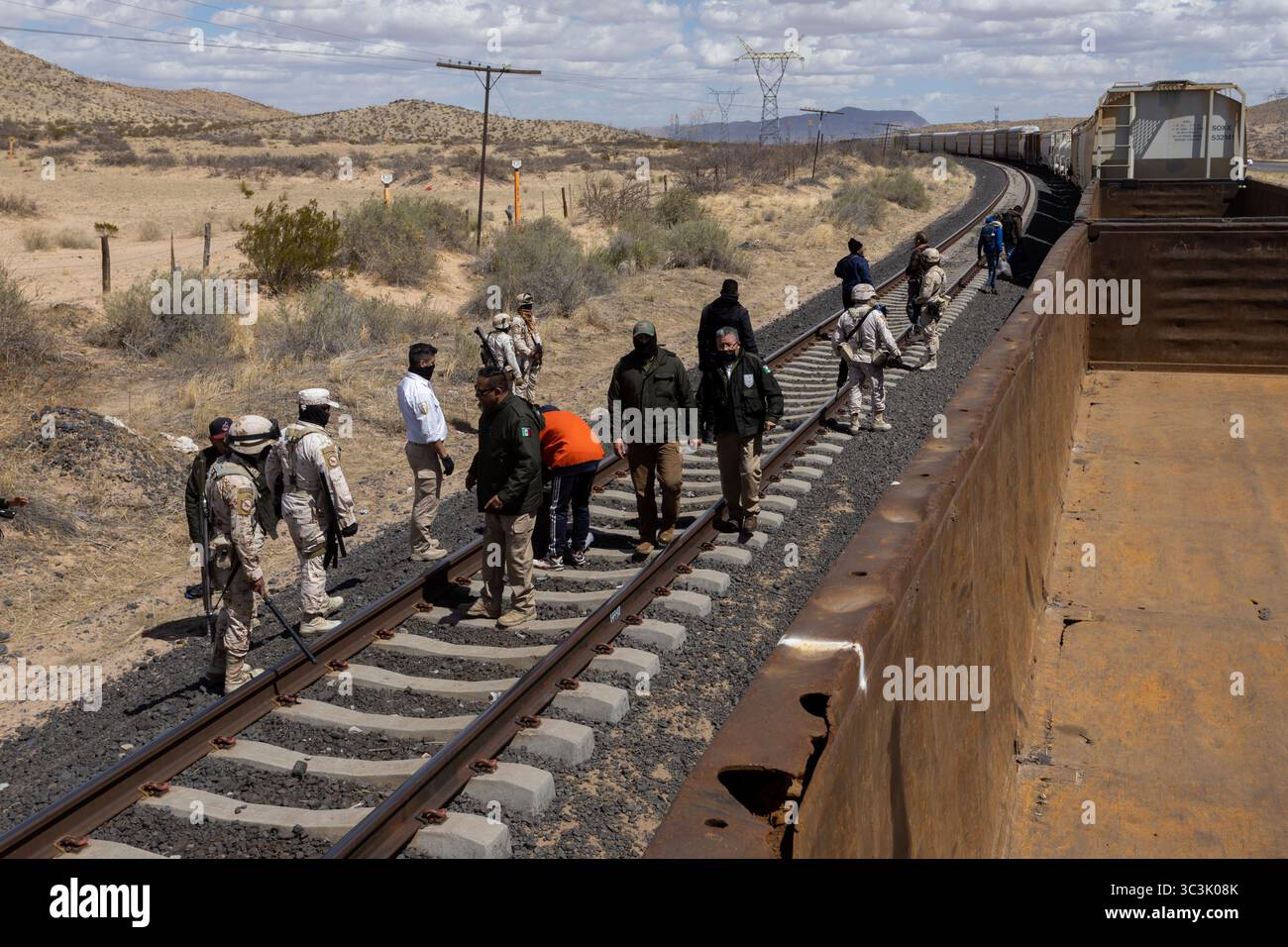 Migranten, die von Beamten entlang der Bahngleise in der Nähe von Ciudad Juarez begleitet werden, zeigen die Herausforderungen der Migration auf. Stockfoto