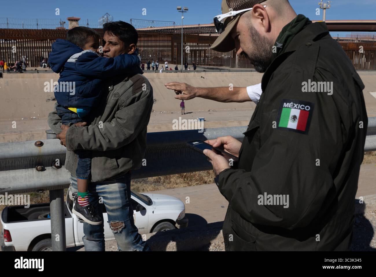 Ein Mann wiegt ein Kind in der Nähe der befestigten Grenze zu Ciudad Juarez und hebt die Herausforderungen der Migration hervor. Stockfoto