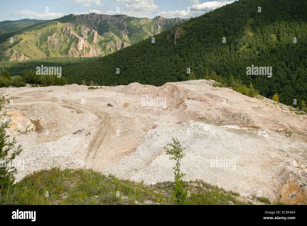 Marmor-Steinbruch im offenen Gruben mit ausgehobenem Gesteinsmaterial vor einem Hintergrund grüner Berge und Wälder. Bergbau- und Industriekonzept. Stockfoto