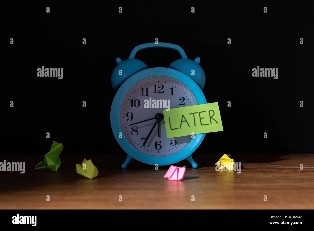 Ein Vintage-Wecker vor dunklem Hintergrund mit einer Notiz „SPÄTER“. Prokrastination, Verzögerung und vergessenes Aufgabenkonzept. Stockfoto