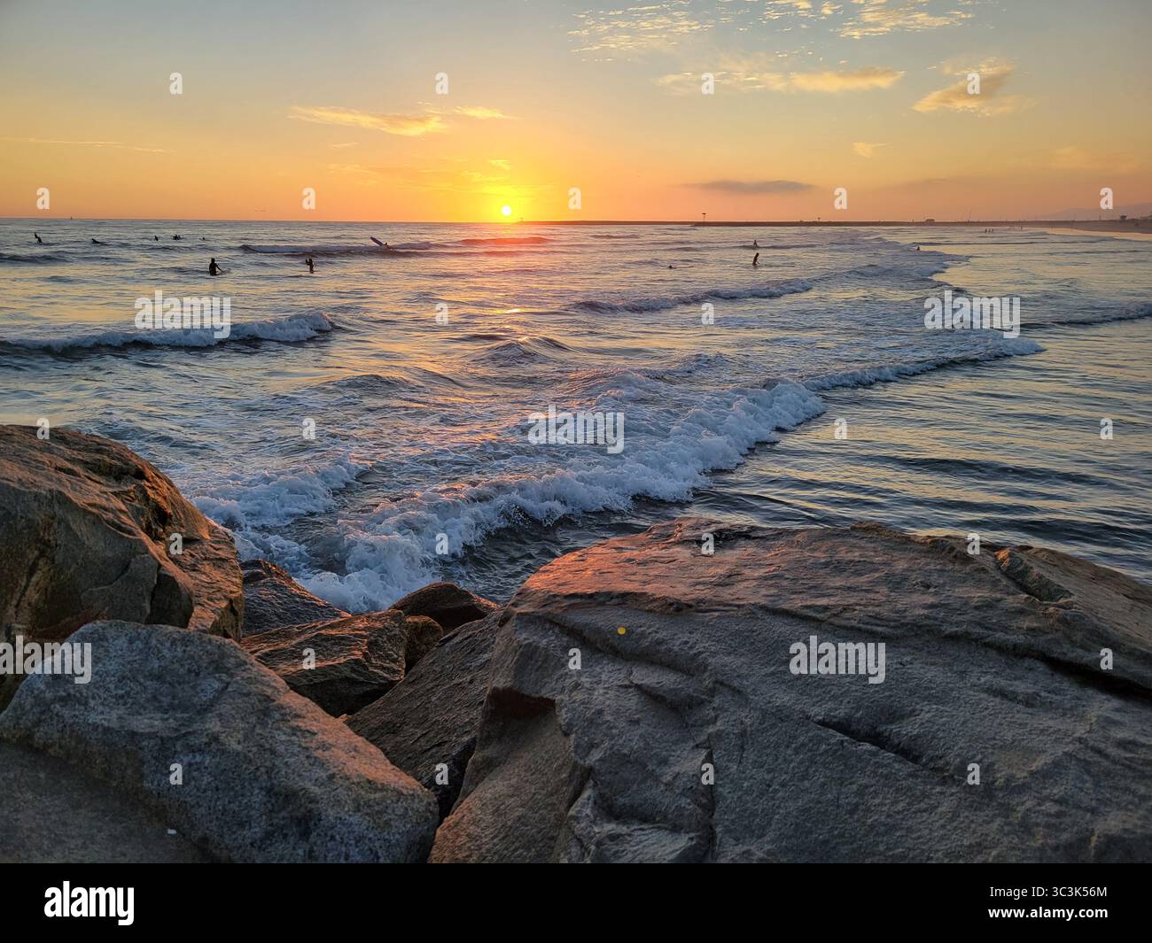 Die Sonne untergeht über dem Pazifik, während einige Schwimmer am Ende des Tages in Kalifornien den Wellen trotzen. - Smartphone-aufgenommenes Stockfoto