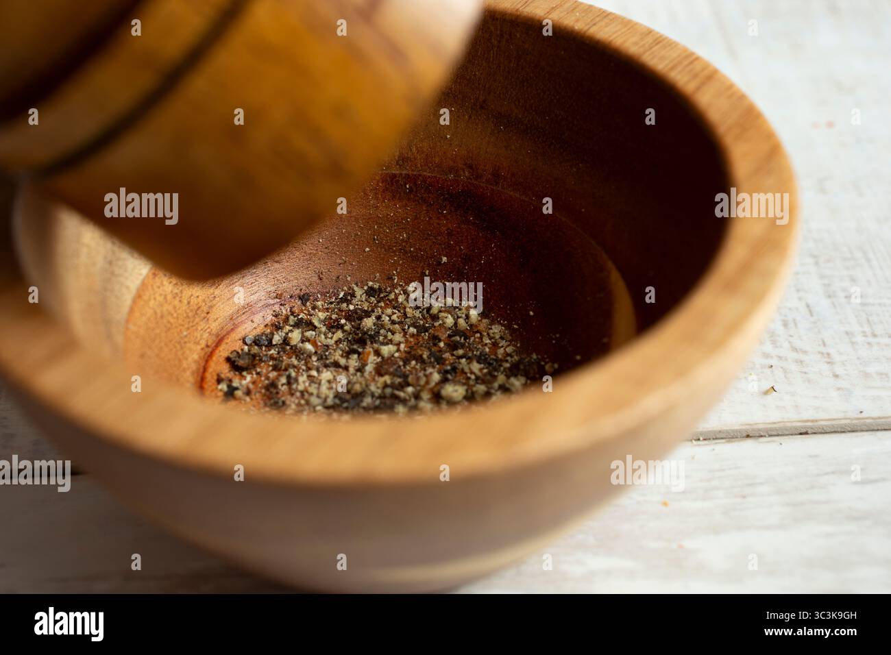 Eine Nahaufnahme einer Pfeffermühle, die schwarzen Pfeffer in einen Gewürzbecher mahlt. Stockfoto