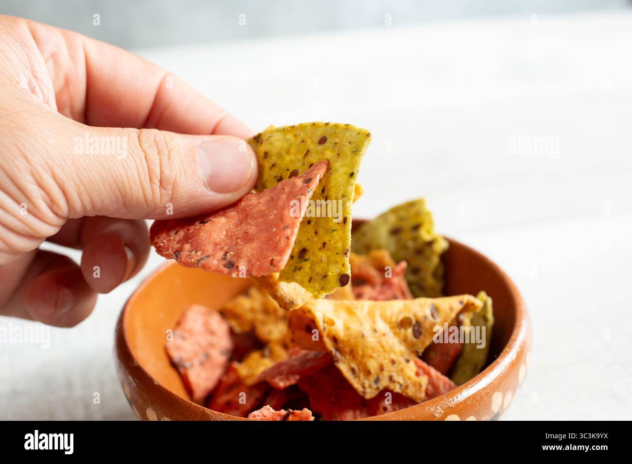Ein Blick auf eine Hand, die ein paar bunte Leinkorntortilla-Chips schnappt. Stockfoto