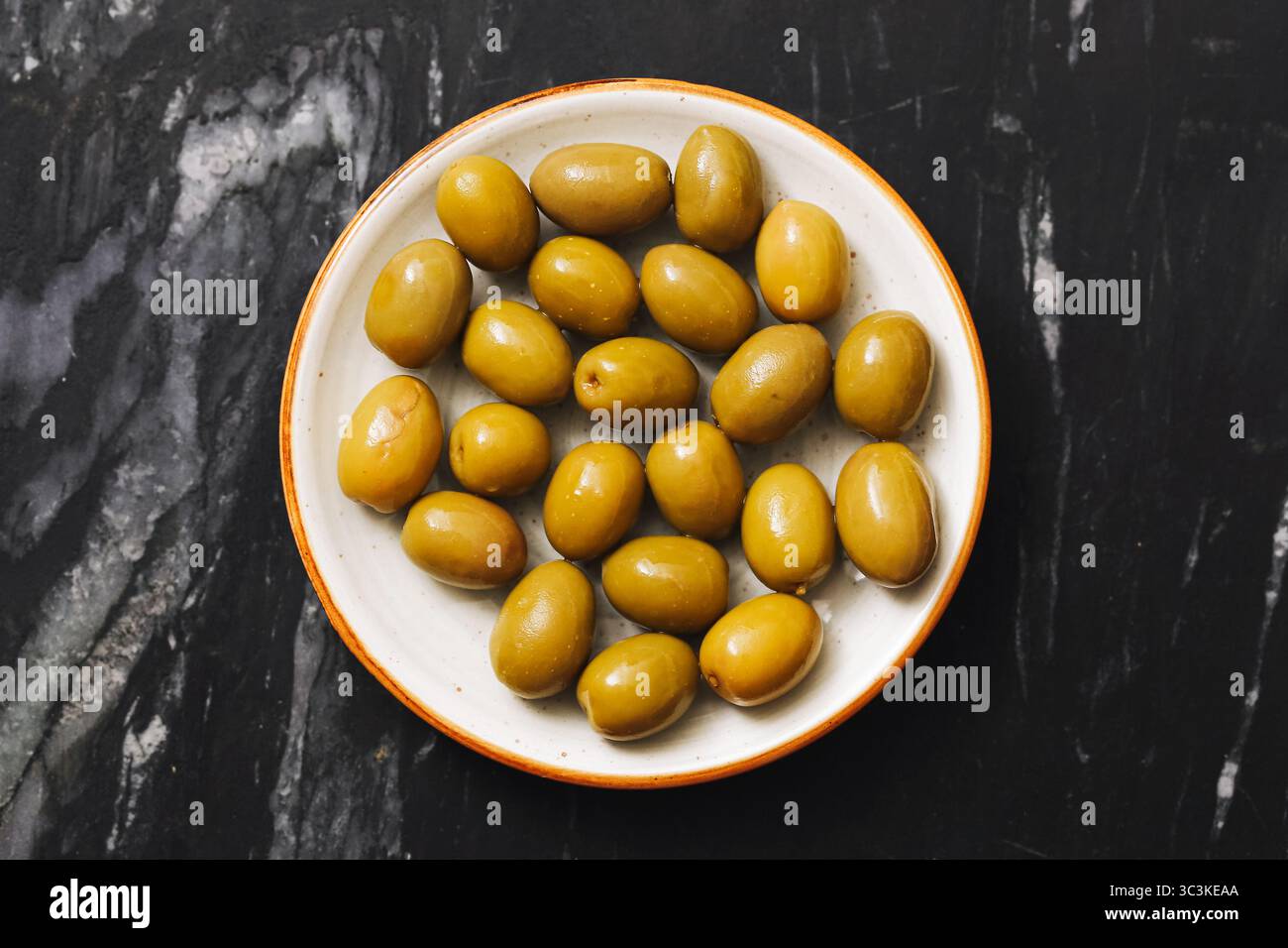 Grüne Oliven in einer Schüssel. Mediterraner Snack auf schwarzer Marmoroberfläche. Gesundes Vorspeisenkonzept. Bio-Obst-Nahaufnahme. Vegetarische Naturkost. Stockfoto