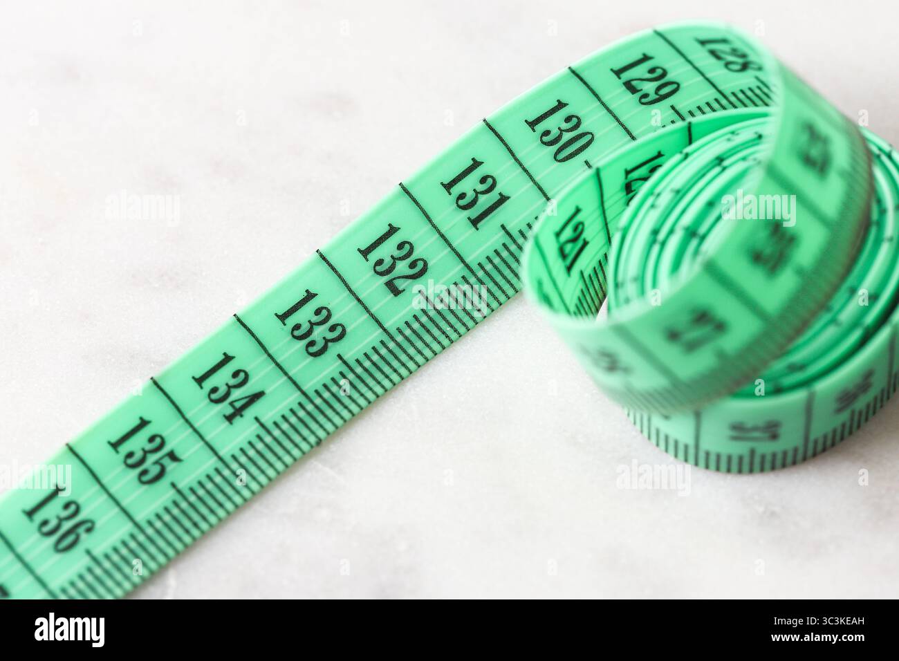 Maßband-Nahaufnahme. Grünes Schneiderzentimeter auf weißer Oberfläche. Flexibles metrisches Werkzeug zum Nähen, Schneiden und Nachverfolgen von Gewichtsverlusten. Stockfoto