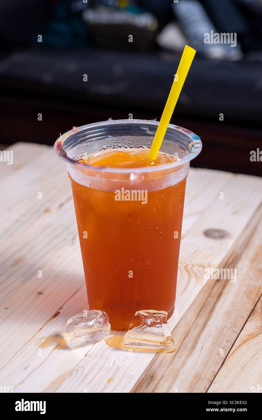 Eistee in einem klaren Plastikbecher mit gelbem Strohhalm. Frische, kalte und süße Getränke, perfekt für Sommer, Street Food oder Erfrischungen Stockfoto