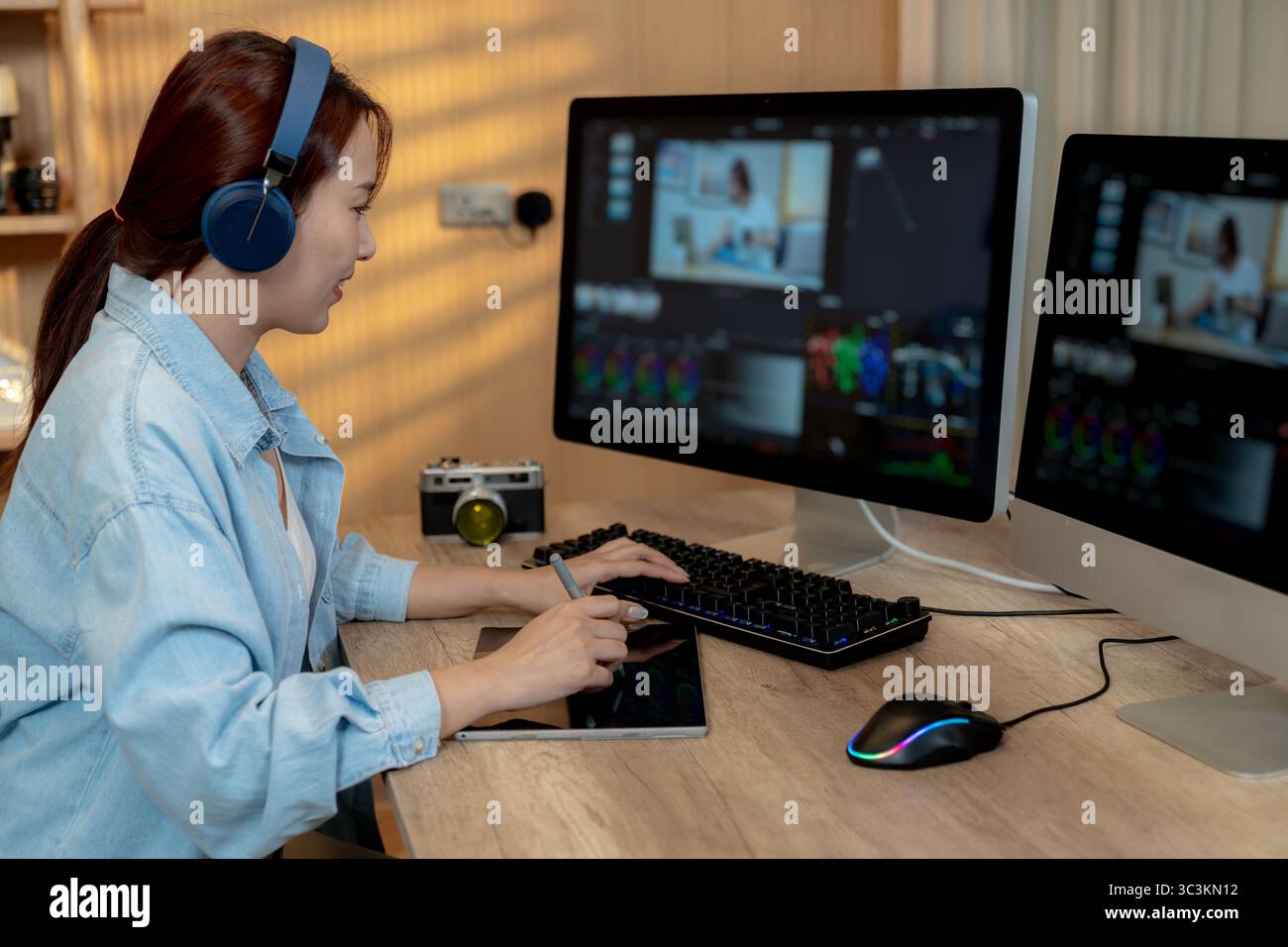 Eine lächelnde junge freischaffende Videoredakteurin, die zu Hause an einem Laptop arbeitet und ihre kreative Arbeit in einer entspannten Umgebung genießt. Stockfoto