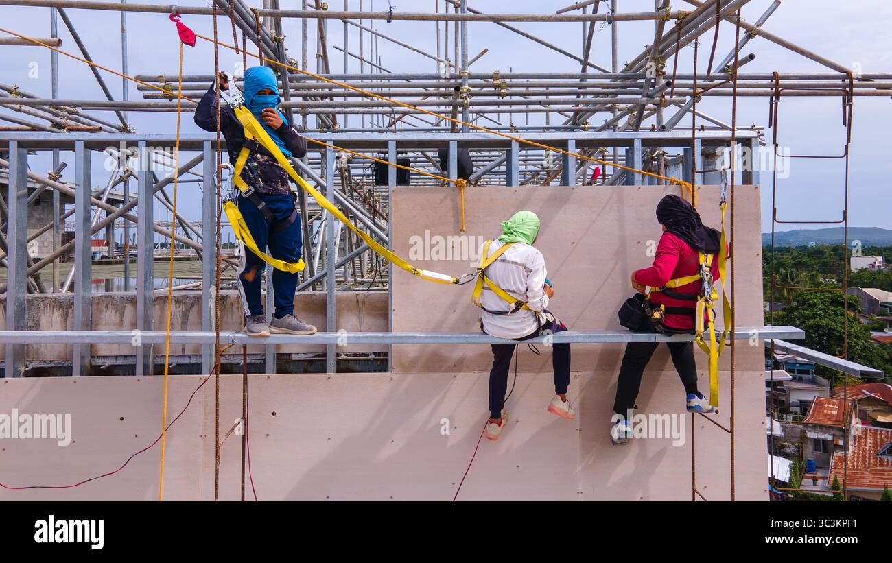 Bauarbeiter installieren Fassadenpaneele in den oberen Ebenen eines Stahlrahmengebäudes, die in der Höhe mit Sicherheitsgurten arbeiten Stockfoto