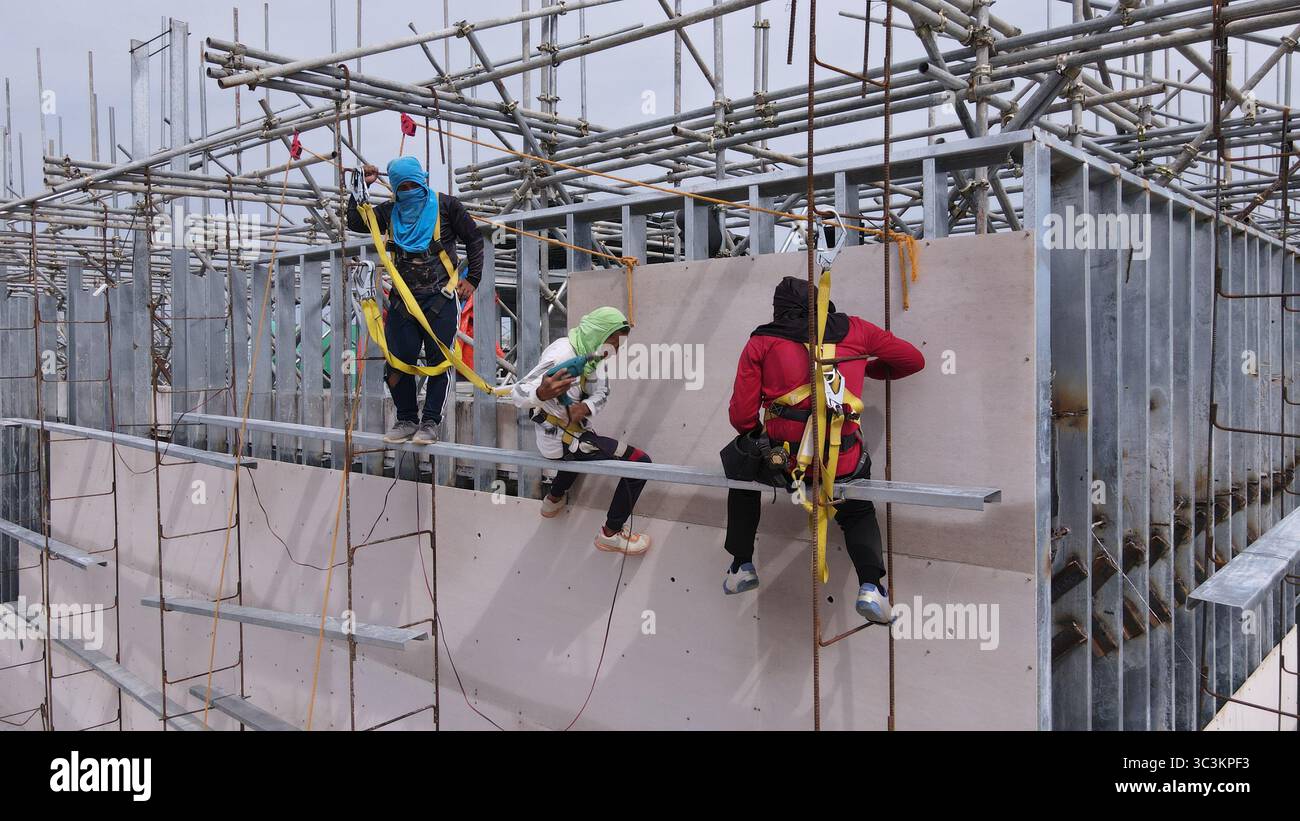 Bauarbeiter installieren Fassadenpaneele in den oberen Ebenen eines Stahlrahmengebäudes, die in der Höhe mit Sicherheitsgurten arbeiten Stockfoto