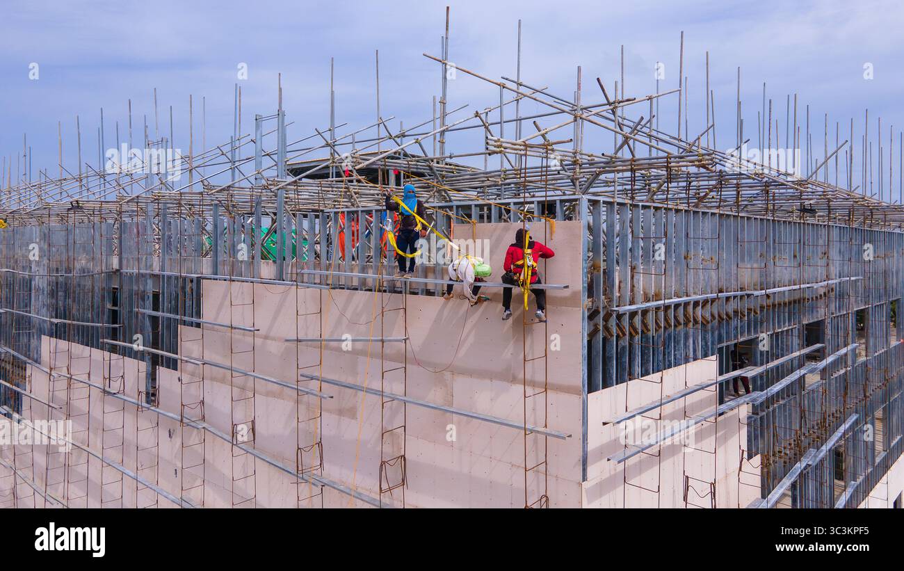 Bauarbeiter installieren Fassadenpaneele in den oberen Ebenen eines Stahlrahmengebäudes, die in der Höhe mit Sicherheitsgurten arbeiten Stockfoto