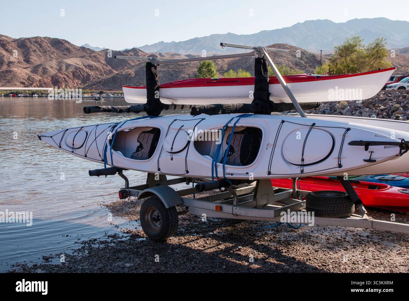 Zwei Kajaks sitzen auf einem Wohnwagen neben dem Colorado River mit Bergen im Hintergrund. Stockfoto
