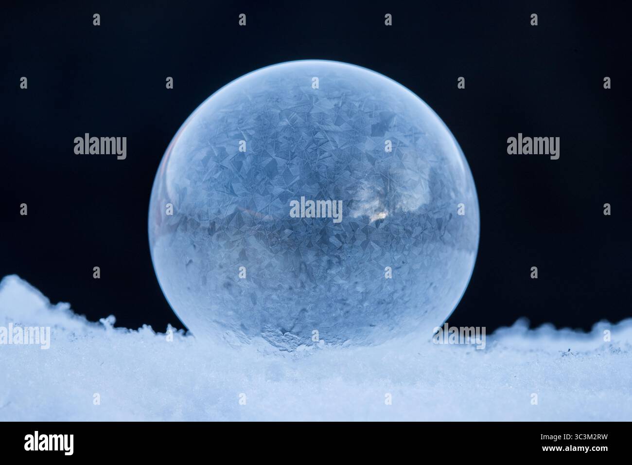 Gefrorene Seifenblase, die auf Schnee ruht, Eiskristall-Muster in der Winterkälte mit dunklem Hintergrund mit Kopierraum Stockfoto