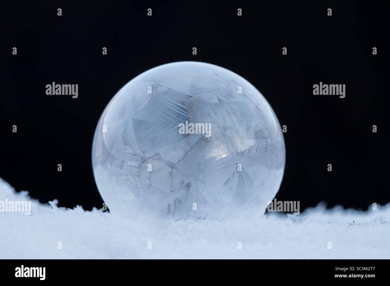 Gefrorene Seifenblase, die auf Schnee ruht, Eiskristall-Muster in der Winterkälte mit dunklem Hintergrund mit Kopierraum Stockfoto