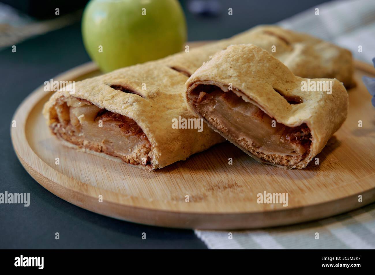 Köstlich gebackener Apfelstrudel gefüllt mit süßen Zimäpfeln auf einem hölzernen Servierbrett mit frischem grünem Apfel als Kontrast Stockfoto