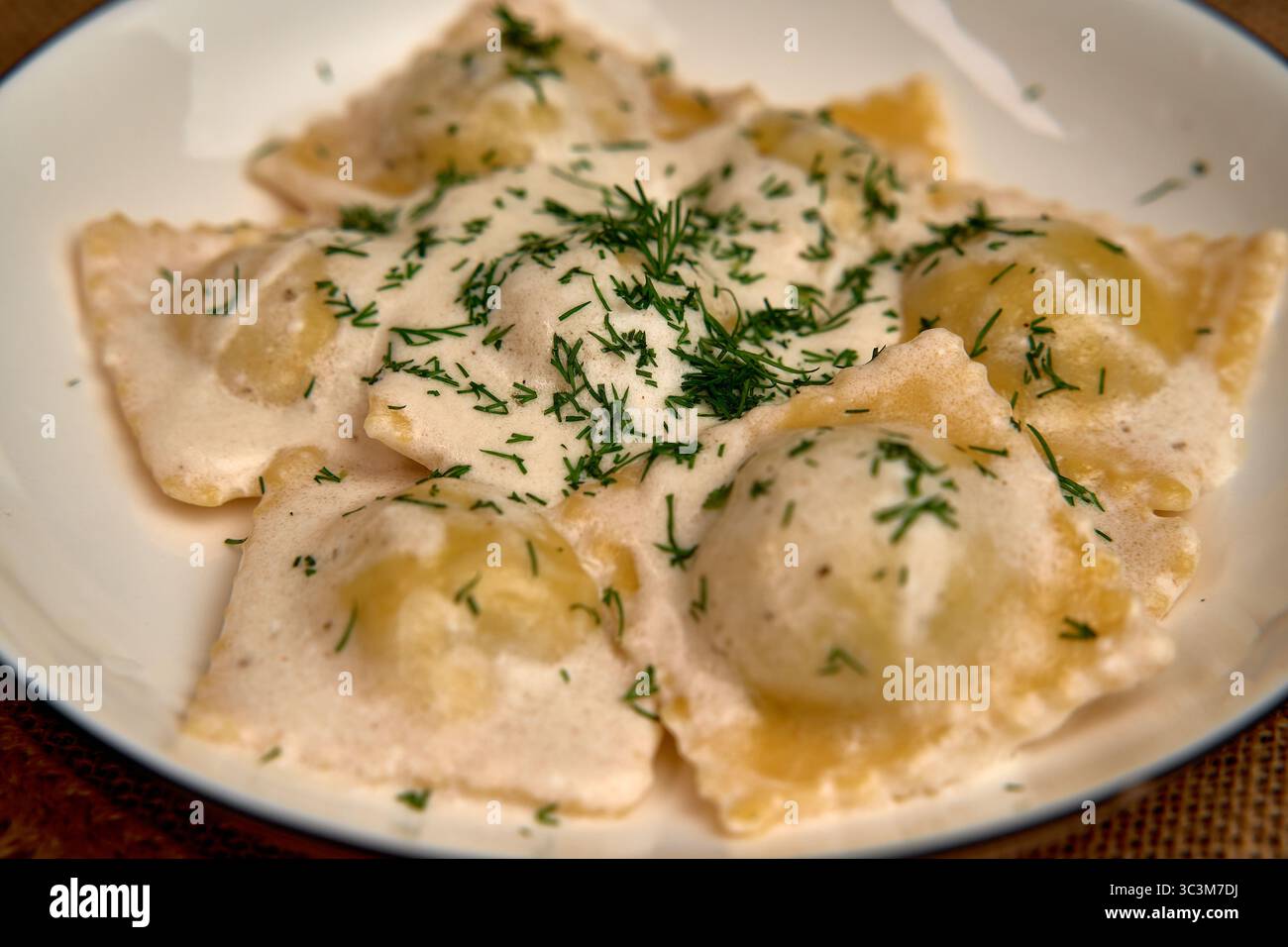 Köstlicher Teller hausgemachter Ravioli mit cremiger Sauce und frischen Kräutern: Ein kulinarischer Genuss für Pasta-Liebhaber Stockfoto