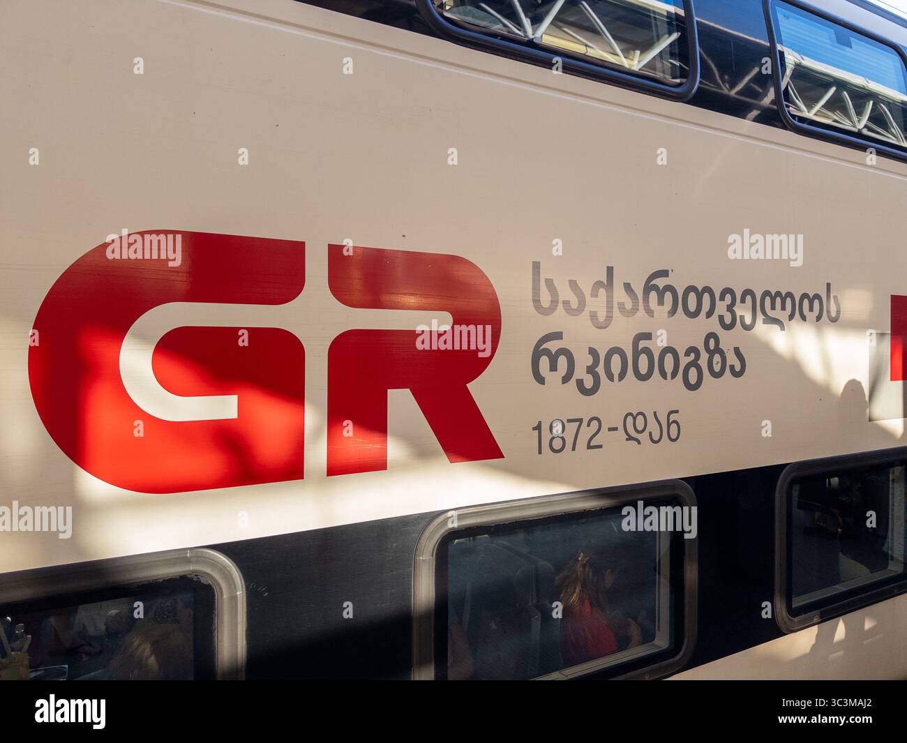 Eine Nahaufnahme eines georgischen Eisenbahnwagens mit dem auffälligen roten „GR“-Logo. Der Text „საქართველოს რკინიგზა“ (georgische Eisenbahn) Stockfoto