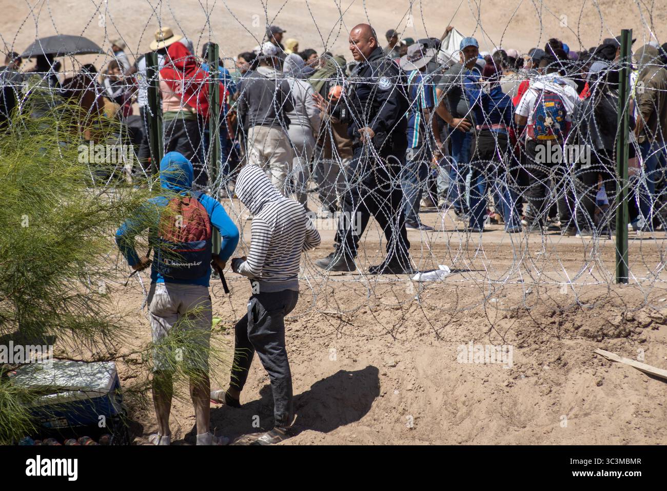 Am Grenzzaun Ciudad Juarez versammeln sich Menschen unter der Aufsicht der Sicherheitskräfte, um die Herausforderungen der Migration zu beleuchten. Stockfoto