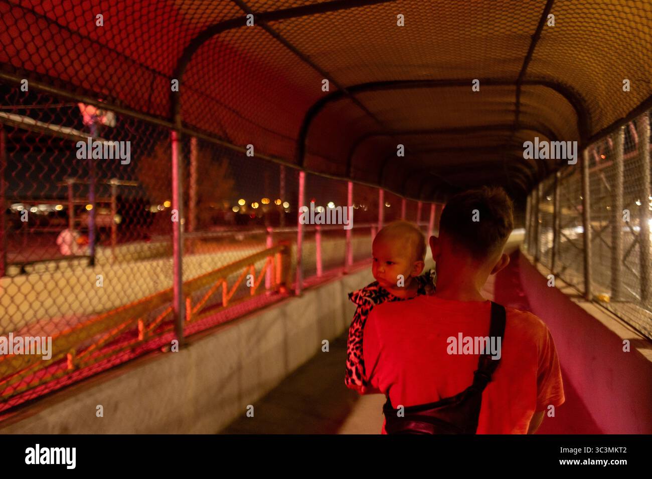 Erwachsene und Kinder überqueren nachts eine beleuchtete Brücke und symbolisieren Hoffnung inmitten der Migrationsherausforderungen in Ciudad Juarez. Stockfoto