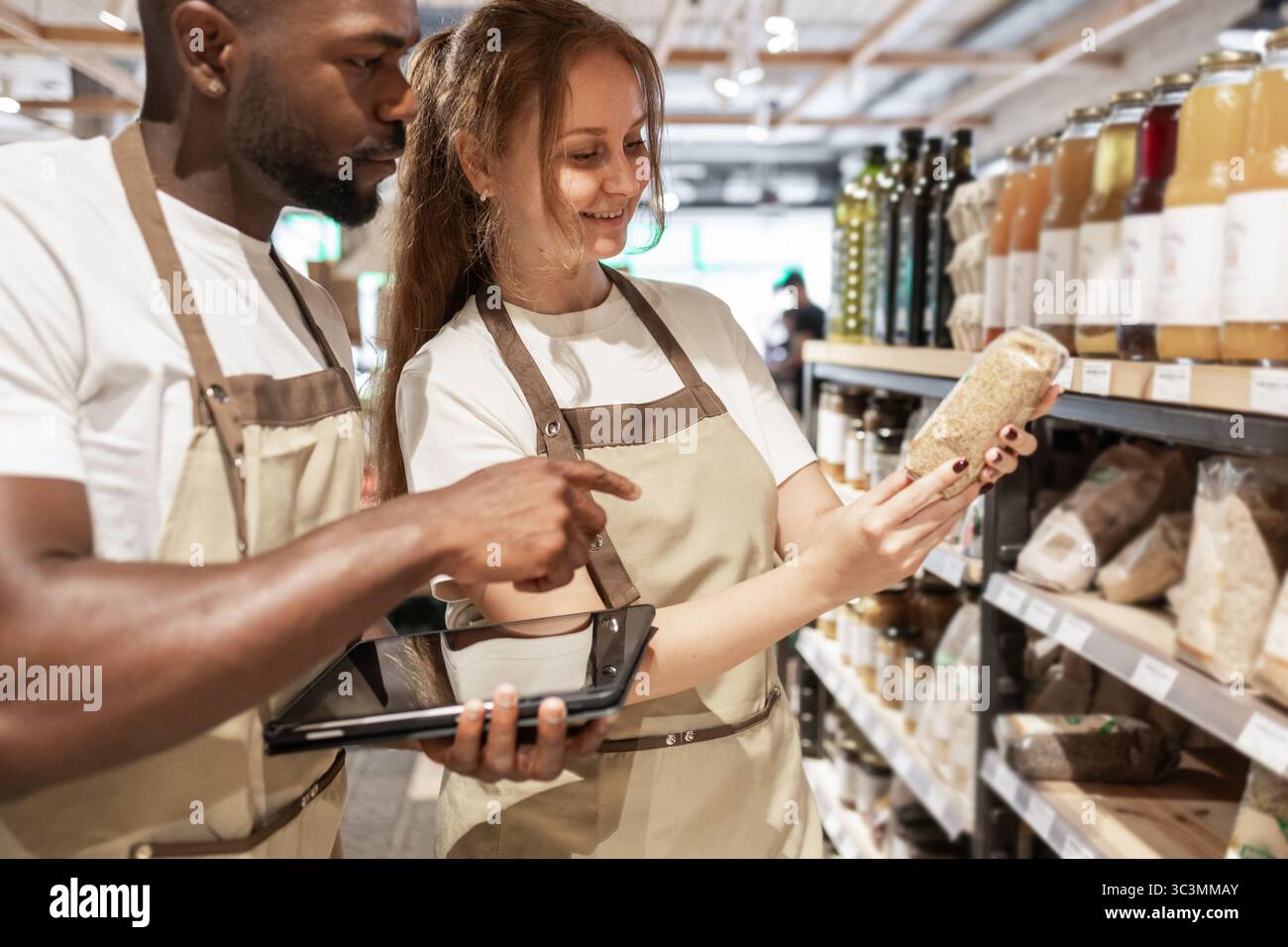 Teammitglieder in einem umweltfreundlichen Geschäft besprechen Produktdetails vor Regalen. Sie konzentrieren sich auf nachhaltige Entscheidungen, was die Bedeutung von g verdeutlicht Stockfoto