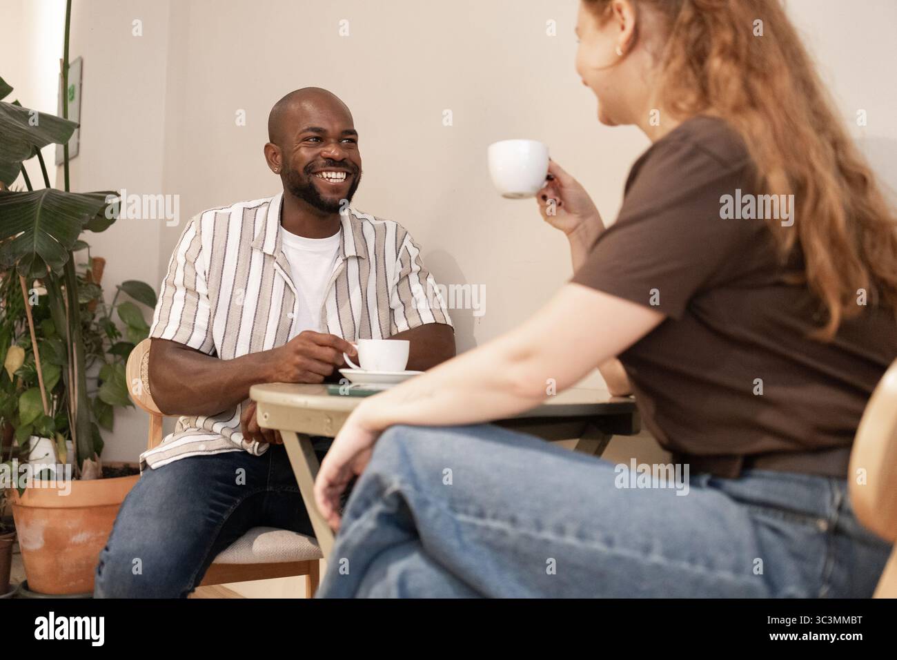 Ein entspannter Moment in einem umweltfreundlichen Café, in dem ein Mann und eine Frau Kaffee und Gespräche genießen. Umgeben von gemütlichem Dekor und üppigen Pflanzen, genießen sie das Stockfoto