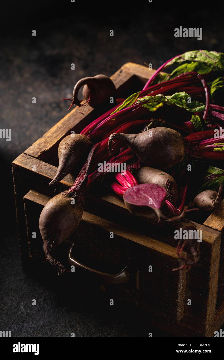 Von oben liegen frische Rote Bete mit lebhaften Stielen und Blättern auf einer rustikalen Holzkiste. Von oben aufgenommen, betonen die Erdtöne und Texturen Stockfoto