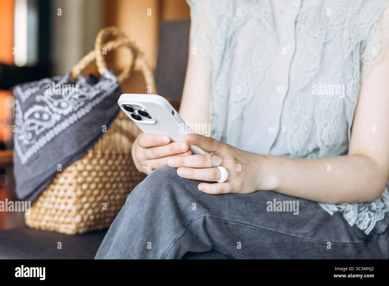Eine Frau sitzt in einem gemütlichen Café und hält ein Smartphone mit beiden Händen. Sie ist lässig gekleidet und neben ihr ist eine gewebte Tasche. Die Szene strahlt Ruhe aus Stockfoto