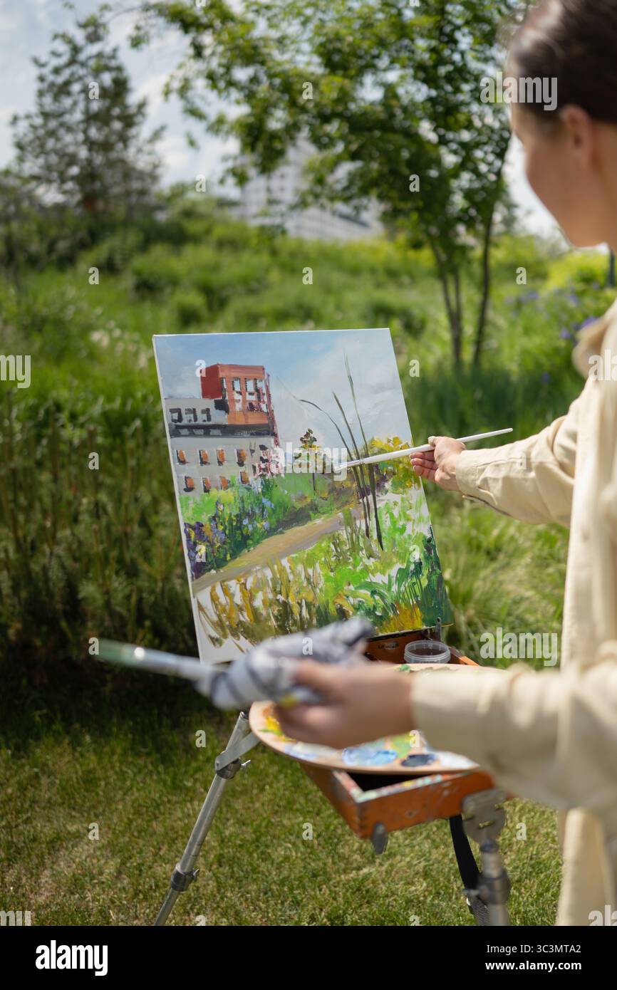 Ein Künstler malte eine lebendige Landschaft auf einer Leinwand im Freien und fängt das Wesen der Natur mit bunten Strichen ein. Die Szene ist voller üppiger Gier Stockfoto