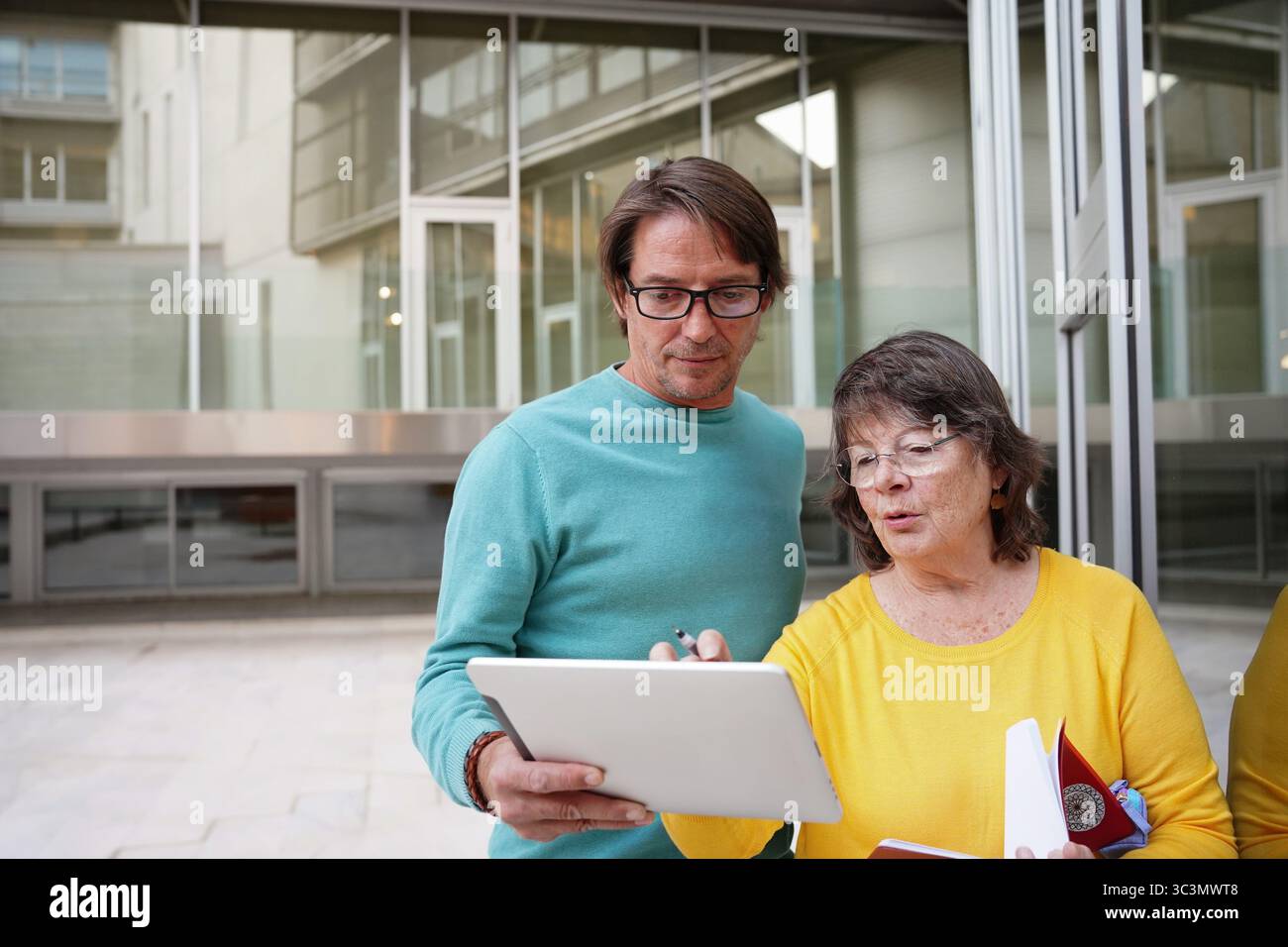 Ein älterer Lehrer und ein Schüler nehmen mit einem digitalen Tablet und einem gedruckten Notebook an einer Lerneinheit im Freien Teil, in der Zusammenarbeit und Modus vorgestellt werden Stockfoto